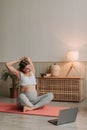 Attractive pregnant woman sit on mat stretching and doing yoga exercises online. Royalty Free Stock Photo