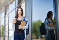 Young female IT student, with books and backpack. Staying outside before lesson and drinking coffee Royalty Free Stock Photo