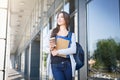Young female IT student, with books and backpack. Staying outside before lesson and drinking coffee Royalty Free Stock Photo