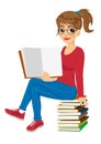 Young female student with glasses sitting on stack of books showing open textbook