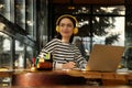 Young female student with laptop and headphones studying at table in cafe Royalty Free Stock Photo