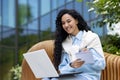 Young female student studying outside university campus, Latin American woman with laptop sitting on bench and recording Royalty Free Stock Photo