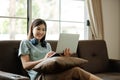 Young female student wearing headphones sits intently and happily studying online on her laptop on the sofa in the Royalty Free Stock Photo