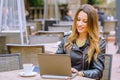Young female smiling while sitting at table in outdoor cafe and browsing modern laptop