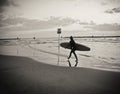 Young female surfer with board walking on the beach, reflected on water, under a cloudy sky