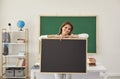 Young female teacher holding empty chalkboard with space for your text at classroom. Happy tutor at work. Back to school Royalty Free Stock Photo