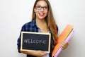 Young female teacher holding folders and blackboard with written welcome Royalty Free Stock Photo