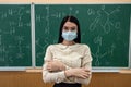 young female teacher in protective mask standing near blackboard
