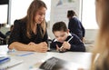 Young female teacher working with a Down syndrome schoolboy sitting at desk using a tablet computer and stylus in a primary school Royalty Free Stock Photo