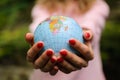 Young female teenager in pink casual clothes with red manicure holding a little globe in her hands. Enviromental Royalty Free Stock Photo