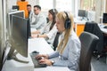 Young female telephone operator with headset working on computer in row in customer service call support helpline center Royalty Free Stock Photo