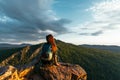 A young female tourist with a backpack admires the sunset from the top of the mountain. A traveler on the background of mountains Royalty Free Stock Photo