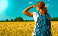 Young female tourist with backpack looking into the distance near a wheat field under the hot summer sky. Royalty Free Stock Photo