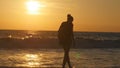 Young female tourist with backpack walking along sea beach at sunset. Beautiful young traveler woman going on ocean Royalty Free Stock Photo