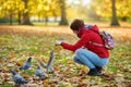 Young female tourist feeding squirrels and pigeon in St James`s Park in London, United Kingdom, on beautiful sunny autumn day Royalty Free Stock Photo