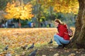 Young female tourist feeding squirrels and pigeons in St James`s Park in London, United Kingdom, on beautiful sunny autumn day Royalty Free Stock Photo