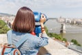 Female tourist looking through city telescope on the old town of Budapest. Travel and view point concept