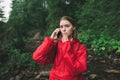 Young female tourist is in mountain forest near the river feeling scared and shocked, talking on the phone, closing her mouth with