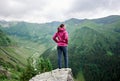 Young female tourist standing on rock edge among magnificent green mountains with grassy slopes Royalty Free Stock Photo