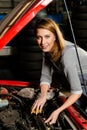Young female trainee fixing car engine in garage