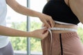 Young female trainer measuring fat layer of overweight woman with waistline at fitness Royalty Free Stock Photo