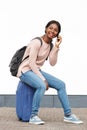 Young female traveler sitting on suitcase and talking on cellphone against white wall Royalty Free Stock Photo