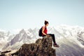 Young female traveller sitting on the edge of rocks. High mountains in background. Woman backpacking. Hiking adventure. Active