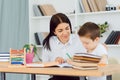 Young female tutor helping little elementary school boy with homework during individual lesson at home