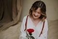 Young female in victorian shirt sitting with rose on the sand and smile