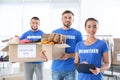 Young female volunteer with clipboard and her team holding boxes full of donations