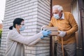 Female volunteer in mask gives an elderly man boxes with food near his house. Quarantined, isolated. Coronavirus covid-19.