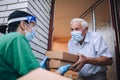 Female volunteer in mask gives an elderly man boxes with food near his house