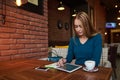 Young female is watching video on digital tablet during rest in modern coffee shop Royalty Free Stock Photo