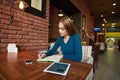 Young female is watching video on digital tablet during rest in modern coffee shop Royalty Free Stock Photo