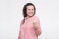 Young female winner in casual pullover raising arm, clenching fist, exclaiming with joy and excitement Royalty Free Stock Photo