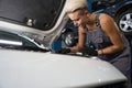 Young female in work overalls repairs a car engine