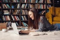 Young woman writer in library at home creative occupation lying writing book on laptop Royalty Free Stock Photo