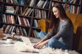 Young woman writer in library at home creative occupation sitting typing on laptop Royalty Free Stock Photo