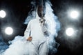 Young fencer athlete wearing fencing costume holding the sword and mask. Isolated on black background with lights