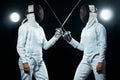 Young fencer athlete wearing mask and white fencing costume. holding the sword on black background with lights.