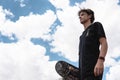 Young skater with the sky in the background and his board in his hands Royalty Free Stock Photo