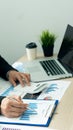 A young financial market analyst works in the office while sitting at a wooden desk. businessman analyzing graph document in hand Royalty Free Stock Photo