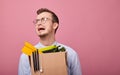 A young fired guy in a sky blue shirt and glasses stands on a pink background with a cardboard box Royalty Free Stock Photo