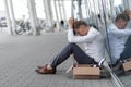 A young fired office worker is sitting under his office.