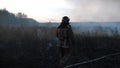 Young fireman in uniform going on burnt grass at countryside. Male fireguard in full equipment walking at meadow after