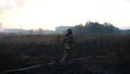 Young fireman in uniform going on burnt grass at countryside. Male fireguard in full equipment walking at meadow after