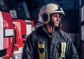 Young fireman wearing protective uniform standing next to a fire engine in a garage of a fire department Royalty Free Stock Photo