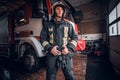 Young fireman wearing protective uniform standing next to a fire engine in a garage of a fire department Royalty Free Stock Photo