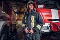 Young fireman wearing protective uniform standing next to a fire engine in a garage of a fire department Royalty Free Stock Photo