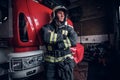 Young fireman wearing protective uniform standing next to a fire engine in a garage of a fire department Royalty Free Stock Photo